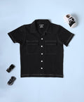 A black, short-sleeved Jacket/Shirt for children features a pointed collar, a full button-down closure with white buttons, and two chest patch pockets with white contrast stitching.